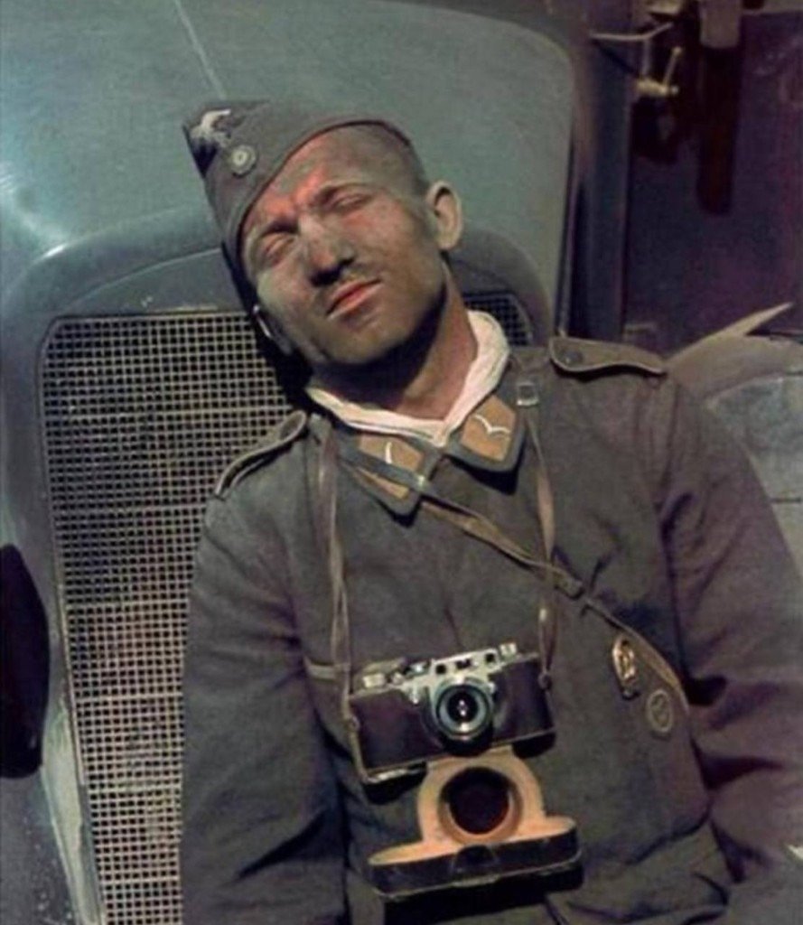 Exhausted soldier with a camera sleeps against a vehicle radiator grille